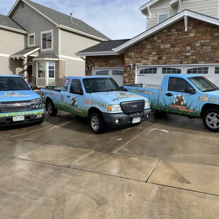 Three Backyard Pooper Scooper branded trucks parked in a residential driveway